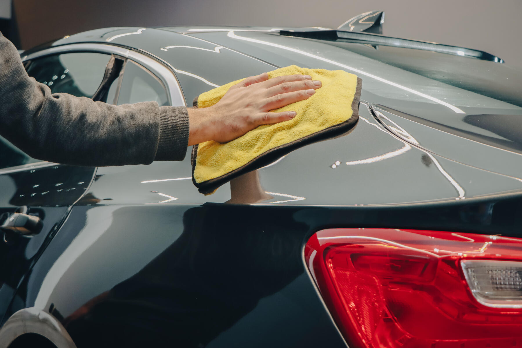 Detailer wiping a black vehicle exterior with a yellow microfiber towel